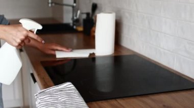 Mutfak tezgahındaki elektrikli sobayı temizliyorum. Ev hanımının ellerini temizler mutfak aletini temizleme spreyiyle temizler. Kadın temizlik, temizlik servisi. Temizlikçi dezenfekte ediyor.