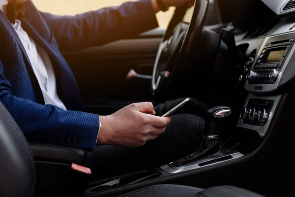 businessman in suit is sitting on driver\'s seat of his luxury car texting on smartphone. Young male taking stop for checking work emails on cell phone in comfortable car while driving to office.