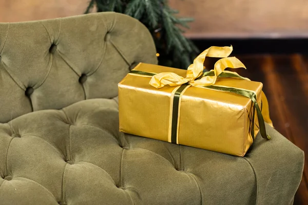 gift box with gold and green ribbons lying on classic velvet green sofa at home. christmas, x-mas, holidays, winter and happiness concept.