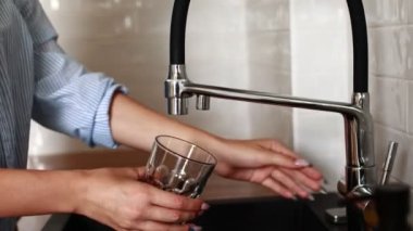 Mutfaktaki cam şişeye taze musluk suyu döküyorum. Kadının eli musluktan cama filtrelenmiş su çekiyor. Su küçük bir filtre musluğundan akar.