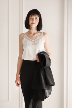 Kendine güvenen esmer iş kadını beyaz arka planda kameraya bakıyor. Siyah takım elbiseli, kısa saçlı, beyaz ceketli, başarılı, dost canlısı bir kadının stüdyo portresi..