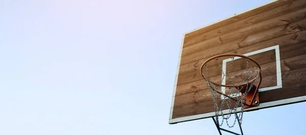 Banner basketball hoop, metal net and wooden backboard for game on blue sky background. Basketball court outdoors. Recreational sport equipment on streetball field alfresco, playground on street