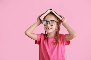 Okul konseptine geri dönelim. Gözlüklü, gülümseyen küçük okul kızı, pembe arka planda izole edilmiş bir çatı gibi kitabı başının üstünde tutuyor. Çocukluk yaşam tarzı konsepti. Okuldaki eğitim. 1 Eylül.