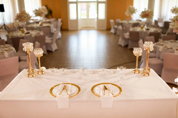 table decoration with pink tablecloth, crystal candlesticks with candles and white pink flowers in restaurant . stylish wedding day. setting table with gold plate, fork and knife.