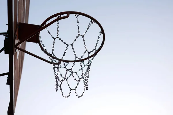 silhouette of basketball hoop with metal net on wooden backboard on sunset sky background. Basketball court outdoors. Recreational sport equipment on streetball field alfresco, playground on street