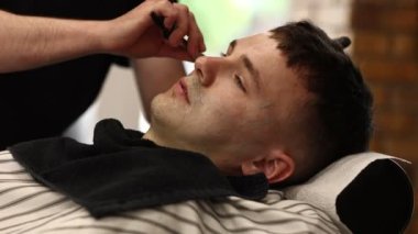 Koruyucu eldivenli bir berber, jiletle genç bir adamı tıraş eder. Bir berber dükkanında ustabaşı bir adamın bıyığını ve sakalını kesiyor. Şık bir berber dükkanı..