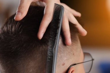 Hands of barber using scissors to cut customer's hair in salon. barber cuts hair, hairstyle. Male customer sitting in chair in hairdressing salon or barbershop. Creating new hair look