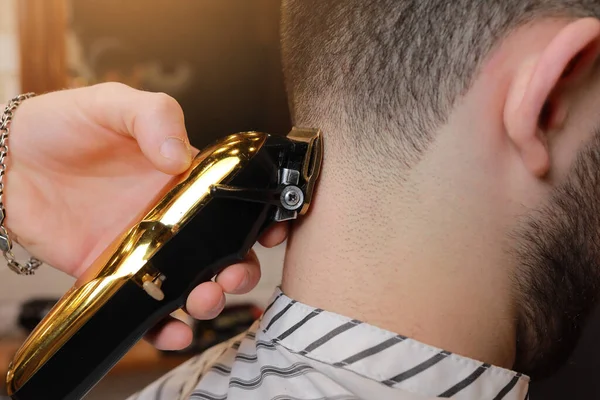 Hairdresser, barber cutting the hair from the back of the client\'s head with a gold electric clipper, razor. Man visiting hairstylist in barbershop.Barber is trimming client hair. Beauty salon.