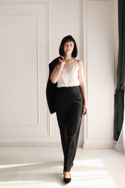 Kendine güvenen esmer iş kadını beyaz arka planda kameraya bakıyor. Siyah takım elbiseli, kısa saçlı, beyaz ceketli, başarılı, dost canlısı bir kadının stüdyo portresi..