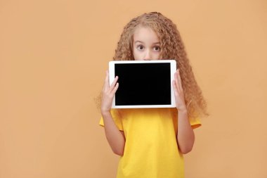 Sarı stüdyo arka planında boş ekranı olan dijital tabletin arkasına saklanan hayret verici çocuk. Heyecanlı liseli kız poz veriyor, maket yapıyor, güzel bir uygulama ilanı veriyor. Yeni Eğitim Uygulaması, Web Sitesi.