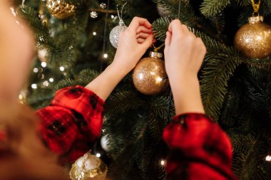 Noel ağacını parlak altın topla süsleyen çocuk elleri. Ağaç xmas gümüşü, altın takılar, çelenkler ve ışıklarla süslenmiş. Noel ve yeni yıl aile bayramı konsepti