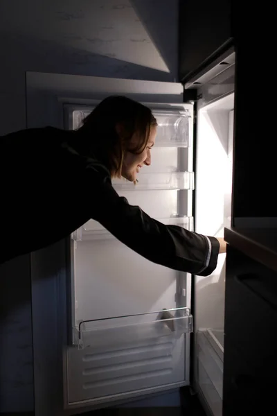 年轻的女人在冰箱里寻找食物 晚上感到饿了 夜袭和不健康的生活方式概念 — 图库照片
