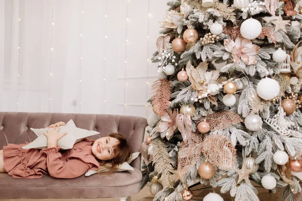 枕の星を持つ笑顔の女の子は カメラを見て 光のガーランドと装飾されたリビングルームでお祝いのクリスマスツリーでソファの上に横たわっています クリスマスの概念 幸せな家族の休日 — ストック写真