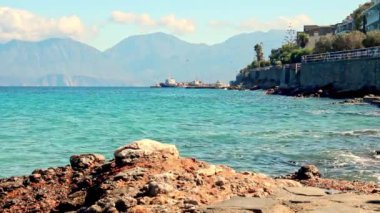 Güzel deniz manzarası, dalgalar kayalık sahil boyunca sıçrıyor ve parlak güneşli bir günde dağ siluetlerinin arka planına karşı yüksek taş seti..