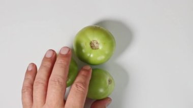 Bir adamın eli beyaz arka planda yeşil domatesler serer. Üst manzara, yakın plan..