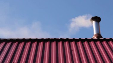 Şömineden bacası, ocağı ve dumanı olan özel bir evin metal çatısı, bir iskan binasının ısıtması. Güneşli bir günde, güzel mavi bir gökyüzünün arka planında