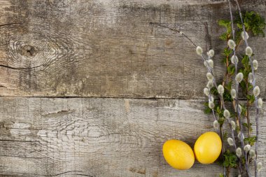 Kırsal bir zemin üzerinde paskalya kompozisyonu, sarı yumurtalar ve yeşil, üst görünümü düz ve kopyalama alanı olan genç bahar dalları..