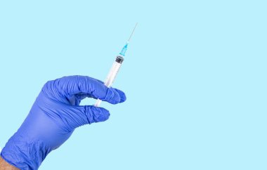 Doktor, mavi ve izole edilmiş Covid-19 aşısı için bir şırınga ile tıbbi eldiven verdi..