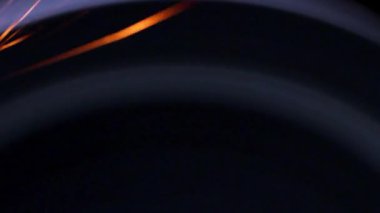 Öğütücü tekerden çıkan parlak sıcak metal kıvılcımları farklı yönlere dağılır. Karanlık bir arka planda, yakın planda..