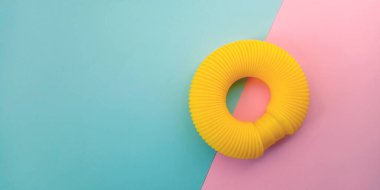 Sarı pop tüpü. Stres önleyici, mavi ve pembe arka planda plastik oyuncak. Fidget kıvrımlı poptube. Üst görünüm, düz görünüm, kopyalama alanı.