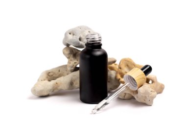 Siyah bir matte şişesinde, taşların çevresindeki izole beyaz arka planda bir pipetle markaların etiketlerinin bir kopyası. Blogger cilt bakımı, yüz, saç ve vücut gereksinimleri.