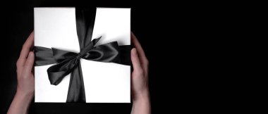 Beyaz bir kutuda, siyah bir yay ile bağlanmış, siyah arka planda genç beyaz bir kızın ellerinde. Kara Cuma için metin yeri olan pankart.