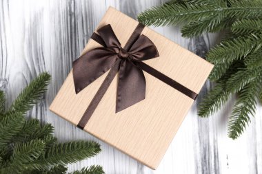 Beyaz ahşap arka planda kahverengi fiyonklu bir hediye kutusu ve Noel ağacı. Yeni yıl hediyesi..