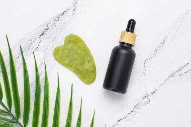 Evde yüz bakımına hazır. Gua sha yeşil taştan yapılmış. Beyaz mermer arka planda kozmetik kaldırma kiti.