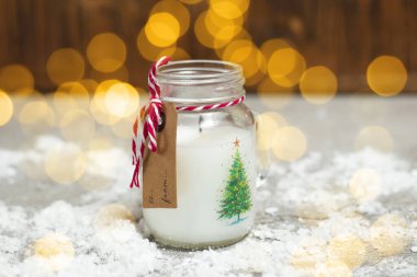 Küçük bir kavanozda stilize edilmiş Noel mumu ve üzerinde altın bokeh ışıkları olan bir etiket. Yeni yıl kartı için kavram.