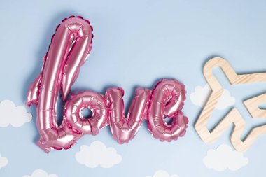 Sevgililer Günü 'nde ya da Anneler Günü' nde seyahat ya da tatil hediyesi olarak. Pembe folyo aşk balonu ve mavi pastel arka planda ahşap bir uçak..