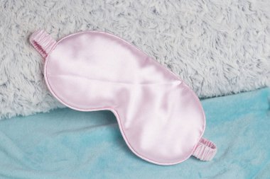 Turkuaz bir arka planda tüylü gri bir yastıkta pembe uyku maskesi. Rahat bir uyku, uyku için yumuşak göz maskesi..