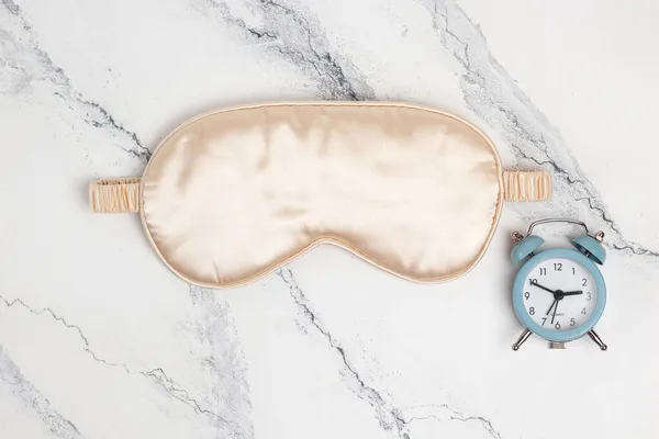大理石の背景に青い小さな目覚まし時計とピンクの睡眠マスク 快適な睡眠 睡眠のための柔らかい目のマスク — ストック写真