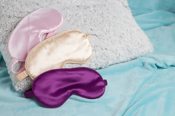 ターコイズ色の背景にふわふわの灰色の枕の上に紫 ピンク 金のスリープマスクが描かれています 旅行のコンセプト 不眠症 リラクゼーション 疲れて眠る — ストック写真
