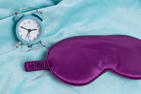 トルコ石の上に小さな青い目覚まし時計を持つ紫の睡眠マスクが背景を果たした よく眠れた — ストック写真
