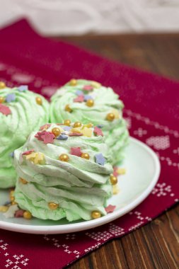 Noel yeşili mojito aromalı marshmallow. Beyaz çay tabağı ve beyaz ahşap arka planda çok renkli şeker parçacıkları serpiştirilmiş. Şenlikli bir şekilde süslenmiş yeni yıl yemeği. Dikey yönelim.