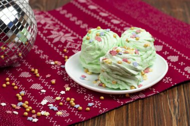 Noel yeşili mojito aromalı marshmallow. Beyaz bir çay tabağına çok renkli şeker serpiştirilmiş. Şenlikli dekore edilmiş Yeni Yıl tatlı yemekleri.
