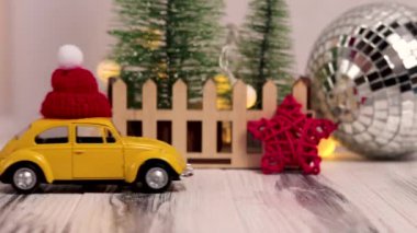 Kırmızı şapkalı sarı bir oyuncak arabayla Noel sahnesi. Kırmızı yıldızlı ve Noel ağaçlı beyaz arka planda sarı oyuncak araba. 29.10.2021 Ukrayna, Vinnytsia