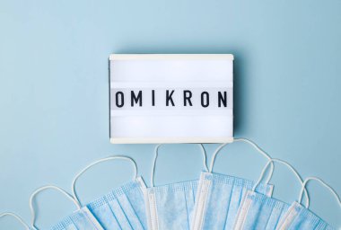 Mavi arkaplan manzarası ve ışık kutusu ve Omicron harfleriyle kaplanmış tıbbi maskeler. Yeni mutasyona uğramış bir koronavirüs türü..
