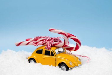 Çatıya şeker kamışları bağlanmış sarı bir oyuncak araba karda duruyor. Noel ve Yeni Yıl takvimleri için kartpostal, afiş ya da baskı. Ukrayna, Vinnytsia - 18.12.2021