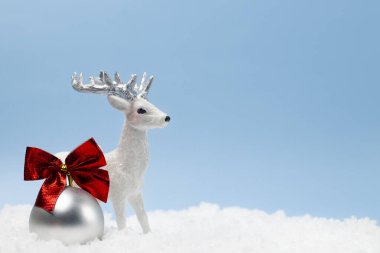 Noel ağacında kırmızı kurdeleli bir topla karda küçük oyuncak geyik. Boşluğu mavi arkaplanda kopyala.