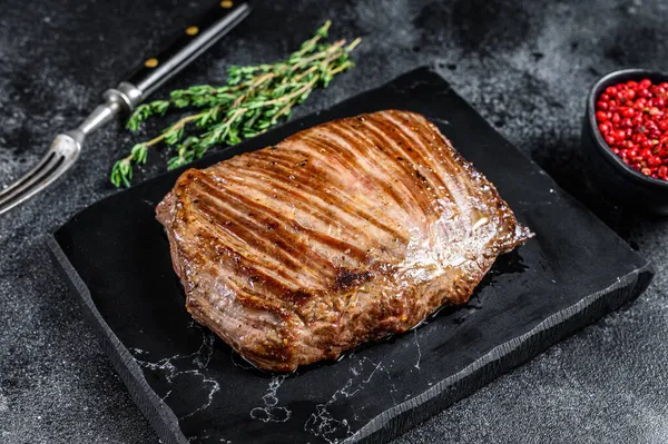 Grillad flankbiff på en marmorbräda. Svart bakgrund. Ovanifrån — Stockfoto