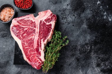 Kurumuş Raw T-bone ya da biftekli biftek, otlar ve tuzlu. Siyah arka plan. Üst Manzara. Boşluğu kopyala
