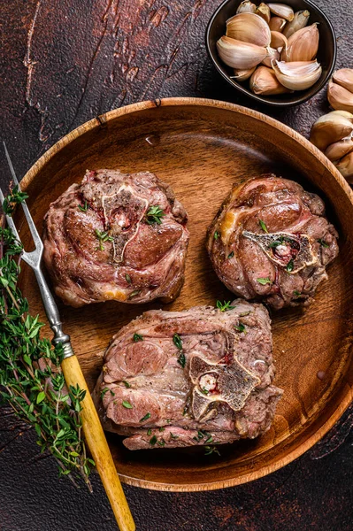 Ahşap bir tabakta kuzu budu bifteği ve otlar. Karanlık arka plan. Üst görünüm