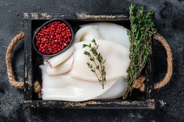 Ahşap tepside otlu çiğ beyaz mürekkep balığı ya da kalamar. Siyah arka plan. Üst görünüm