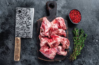 Çiğ kuzu eti yahnisi. Tahta kasap tahtasında ve satırda kemik var. Siyah arka plan. Üst görünüm