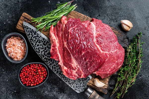 Çiğ Chuck 'ın gözü siyah Angus bifteği kasap tahtasının üzerinde bıçakla yuvarlandı. Siyah arka plan. Üst görünüm