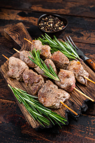 Shish kebab on skewers with herbs on a wooden board. Dark wooden background. Top view