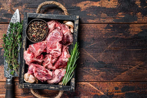 Raw lamb or goat meat diced for stew with bone. Dark wooden background. Top view. Copy space