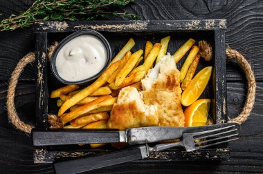 Patates kızartması ve ahşap tepside tartar soslu haşlanmış balık ve patates kızartması. Siyah ahşap arka plan. Üst görünüm