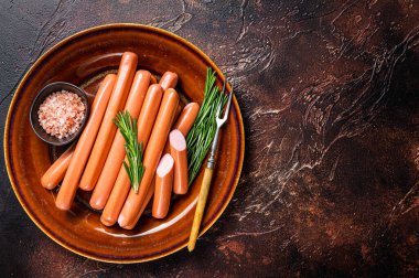 Frankfurter raw sausages in a rustic plate with herbs. Dark background. Top view. Copy space clipart
